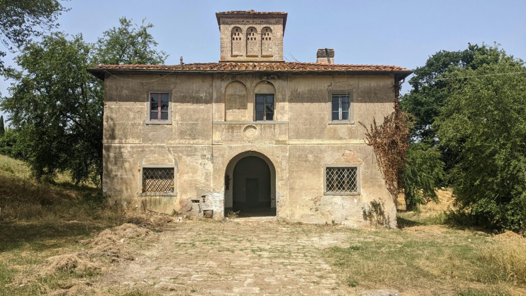A rustic Tuscan farmhouse with a charming archway under the summer sun.